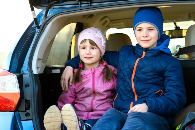 Twee gelukkige kinderenjongen en meisjeszitting samen in een autoboomstam. Vrolijke broer en zus knuffelen elkaar in de bagageruimte van het gezinsvoertuig. Weekend reizen en vakanties concept.