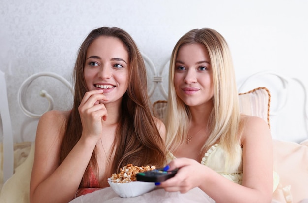 Twee gelukkige lachende vriendinnen eten popcorn in bed