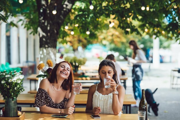 Twee gelukkige lachende vrouwen die water drinken in café