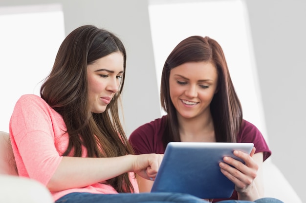 Twee gelukkige meisjes die op een bank zitten die een tabletpc met behulp van