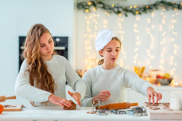 Twee gelukkige meisjes koken peperkoek maken, koekjes van peperkoekdeeg snijden, plezier maken.