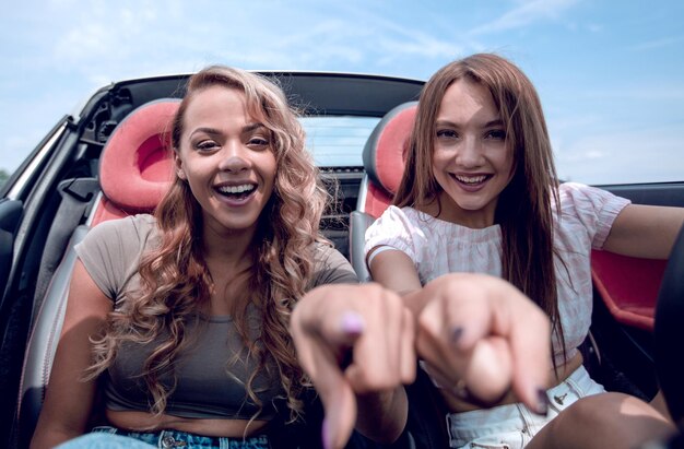 Twee gelukkige meisjes zitten in de auto en wijzen naar jou