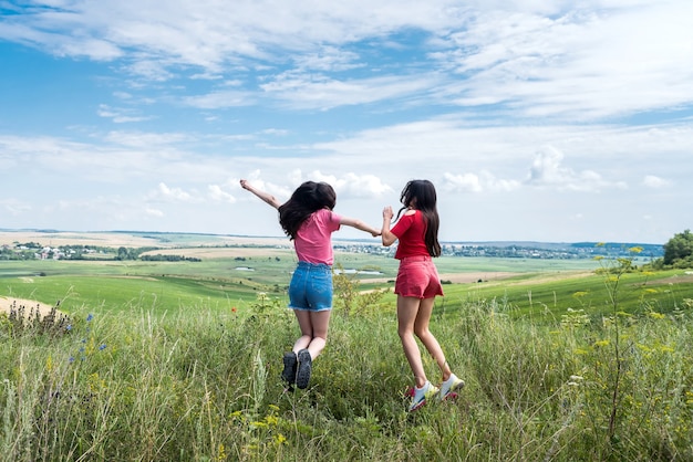 Twee gelukkige slanke glimlachende jonge vrouwen die samen op landelijk gebied op de blauwe hemel springen