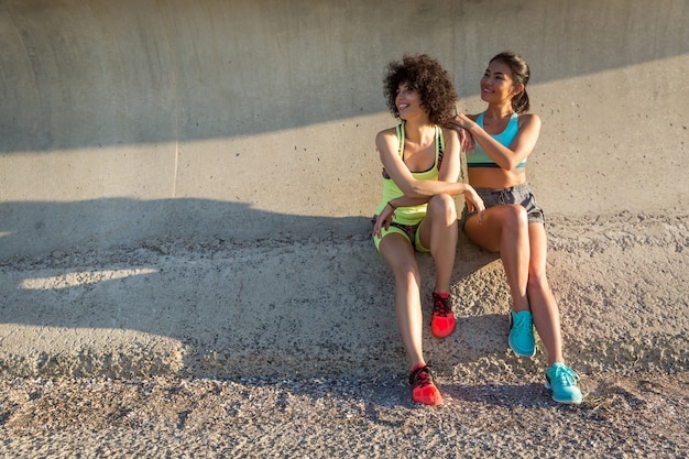 Twee gelukkige sportieve vrouwen in sportkleding zitten samen