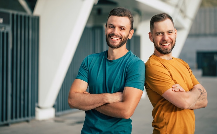 Foto twee gelukkige vrienden of broers in kleurrijke t-shirts staan rug aan rug met gekruiste armen buitenshuis