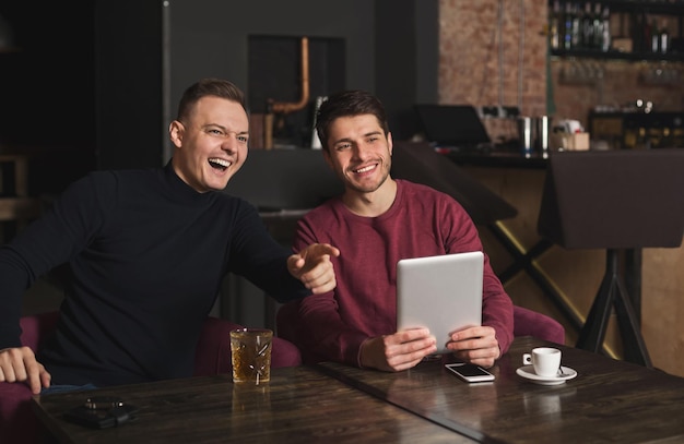 Twee gelukkige vrienden surfen op sociale netwerken op digitale tablet en lachen. Technologieën, online communicatie en internetverslaving, kopieerruimte