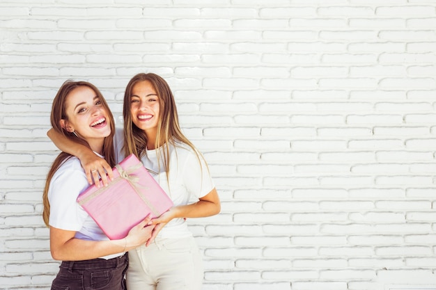 Twee gelukkige vrouwelijke vrienden met verjaardagsgift voor bakstenen muur