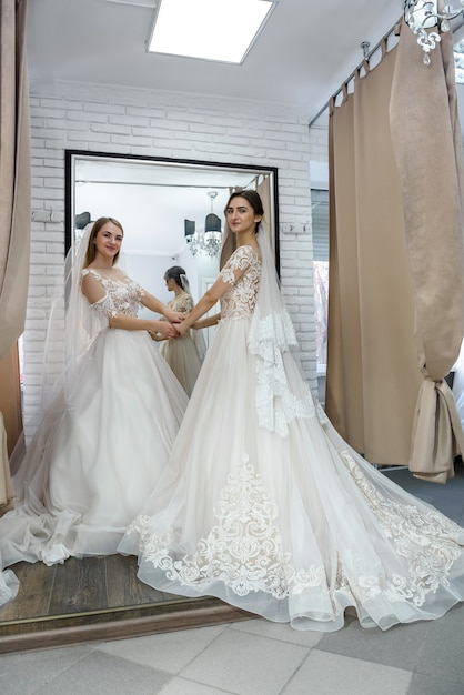 Twee gelukkige vrouwen in trouwjurken poseren in salon