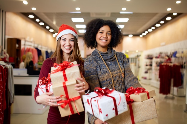 Twee gemengd ras vrouwen met geschenkdozen in handen in de winkel Multi-etnische meisjes lachend met cadeautjes op Kerstmis Nieuwjaar verkoop Kaukasische en Afro-Amerikaanse vrouwtjes winkelen cadeautjes voor vakantie