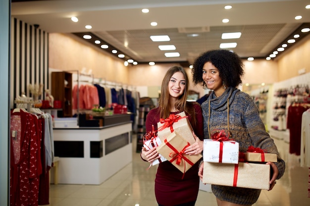 Twee gemengd ras vrouwen met geschenkdozen in handen in de winkel Multi-etnische meisjes lachend met cadeautjes op Kerstmis Nieuwjaar verkoop Kaukasische en Afro-Amerikaanse vrouwtjes winkelen cadeautjes voor vakantie