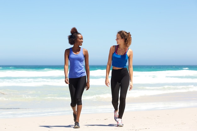 Twee geschikte jonge vrouwen die op strand lopen