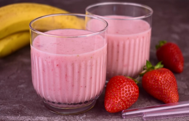 Twee glaasjes aardbeiensmoothies met daarnaast een banaan en banaan