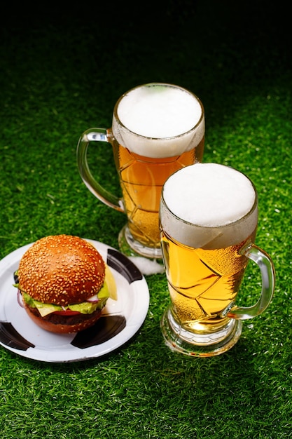 Twee glazen bier en hamburger op groen gras