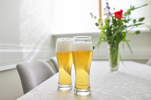 Twee glazen bier op tafel, thuis tafel met stoelen in de buurt van raam.