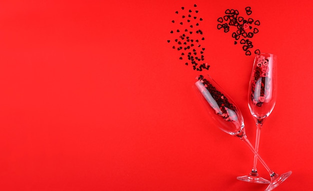 Twee glazen champagne gevuld met hartvormige pailletten op een rode achtergrond Valentijnsdag.