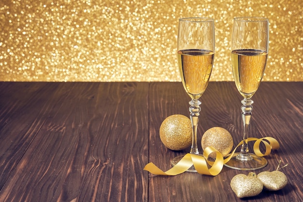 Twee glazen champagne op een bruine houten tafel met gouden kerstballen en ongericht glinsterende gouden achtergrond