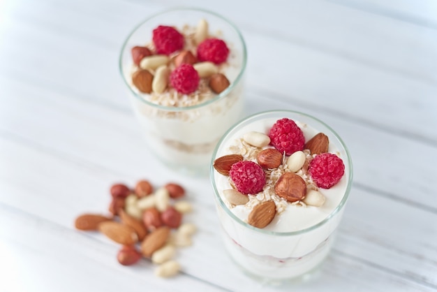 Twee glazen Griekse yoghurt met frambozen, havermoutvlokken en noten