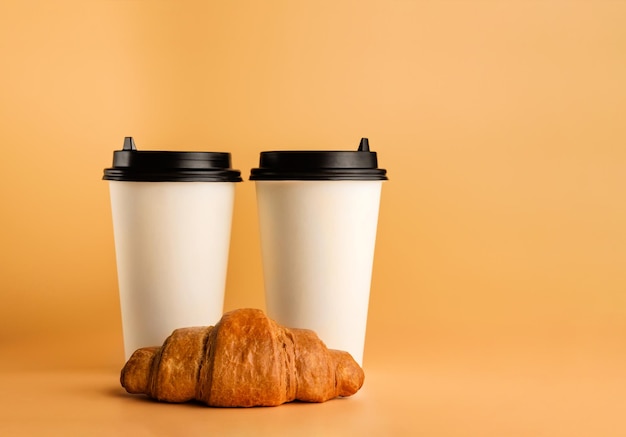 Twee glazen koffie en een croissant op een crèmekleurige achtergrond met kopieerruimte.