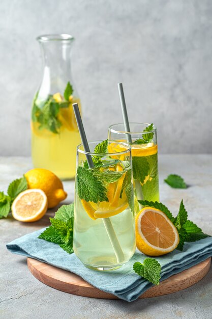 Twee glazen limonade en een karaf op een grijze achtergrond met citroenen. Verticale weergave. Zomers drankje.