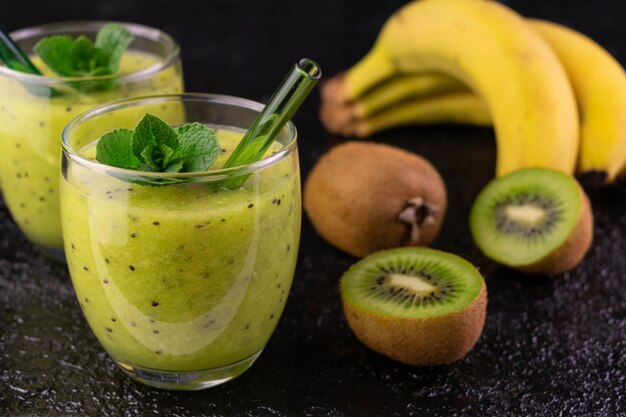 Twee glazen met kiwi smoothie en banaan op een zwarte backgroundCloseup