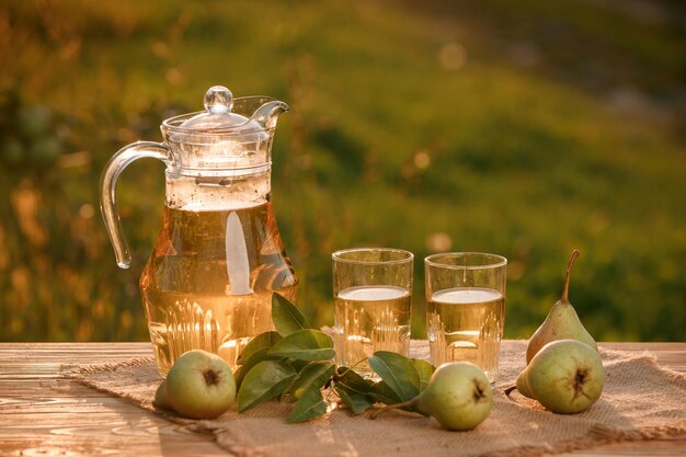 Twee glazen met perensap en mand met peren op houten tafel met natuurlijke boomgaardachtergrond op zonsonderganglicht Vegetarische fruitcompositie