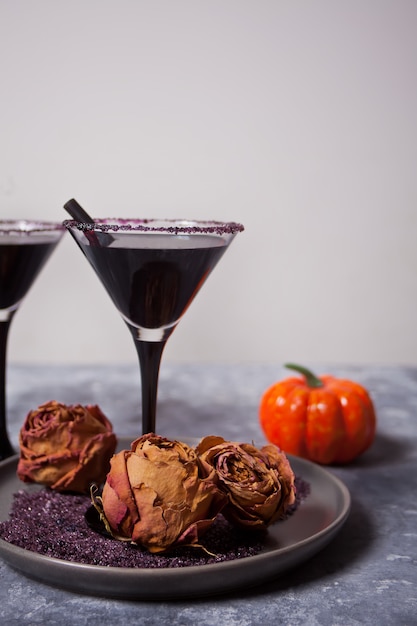 Twee glazen met zwarte cocktail, gedroogde rozen, pompoen voor Halloween-feest op de donkere achtergrond