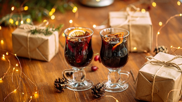 Twee glazen mokken glintwine met ambachtelijke cadeautjes en guirlande lichten op de houten tafel