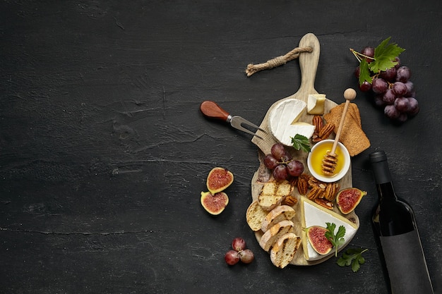 Twee glazen rode wijn en een smakelijk kaasplateau met fruit, druif, noten en geroosterd brood op zwart bureau.