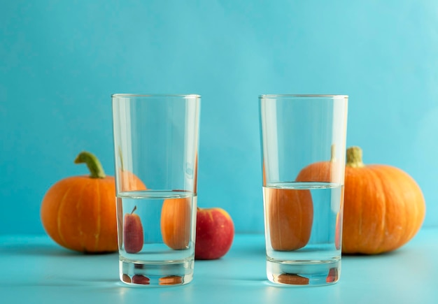 Twee glazen schoon water erachter zijn pompoenen en een appel op een blauwe achtergrond