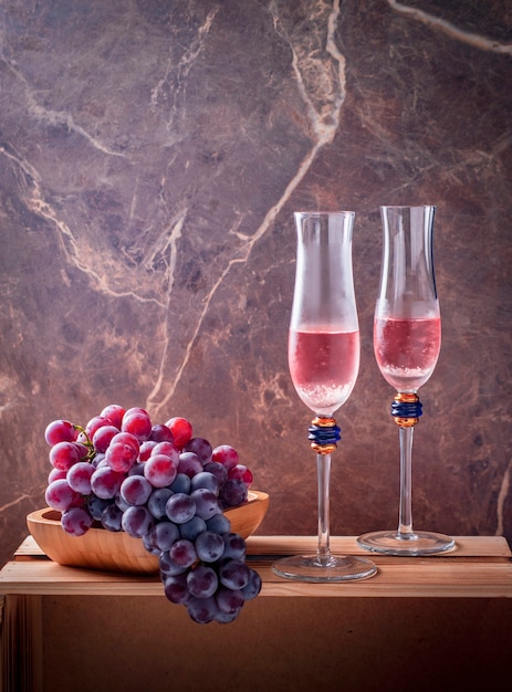 twee glazen sprankelende roos op een houten kist met trossen druiven in een houten dienblad dramatische lichte marmeren achtergrond