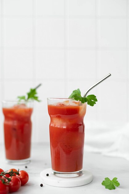 Foto twee glazen tomatensap met een takje peterselie en peper op een witte tafel