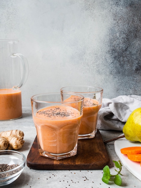 Twee glazen verse gezonde wortel, peer, gember smoothie met chiazaden op grijze achtergrond