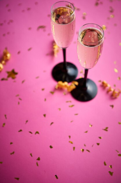 Twee glazen vol mousserende champagnewijn met gouden decoratie van confetti en serpentines op roze achtergrond Top uitzicht met kopieerruimte Feestelijk of feestconcept