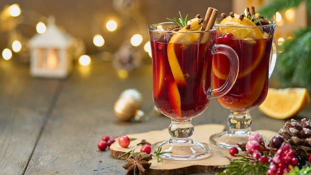 Twee glazen warme rode glühweindranken met kardemom, kaneel, kruidnagel, sinaasappel, anijs, cranberry, dennennaalden. Seizoensgebonden winterdrankje. Kerst decor. Selectieve aandacht, onscherpe achtergrond