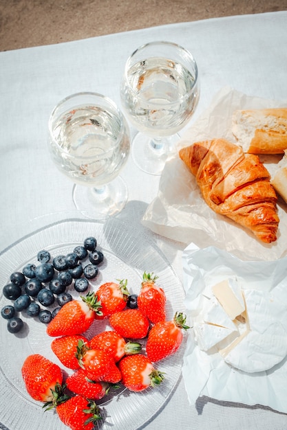 Twee glazen witte wijn en bessen, gebak, brood en camembert kaas op witte tafel set-up