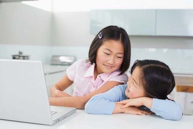 Twee glimlachende jonge meisjes met laptop in keuken