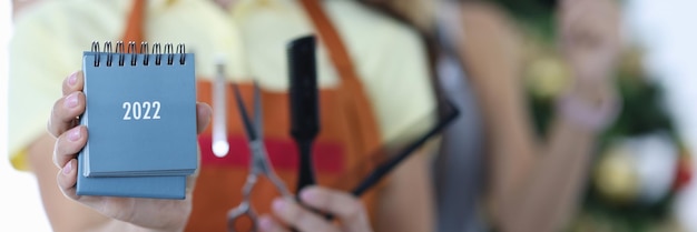 Twee glimlachende vrouwelijke kappers in uniformen houden kalender en schaar vast met een kam kapper