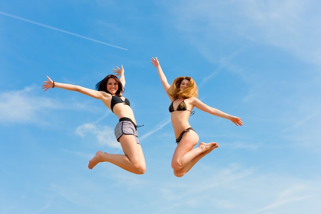 Twee glimlachende vrouwen die in zwembroek hoog in de hemel springen