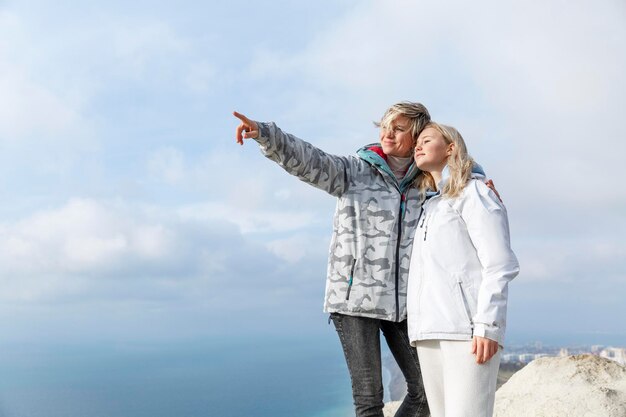 Twee glimlachende vrouwen in sportjassen staan op de top van een berg boven de zee actieve levensstijl energie en gezondheid