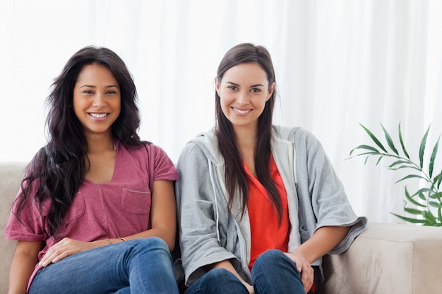 Twee glimlachende vrouwen zitten samen op de laag terwijl het bekijken de camera