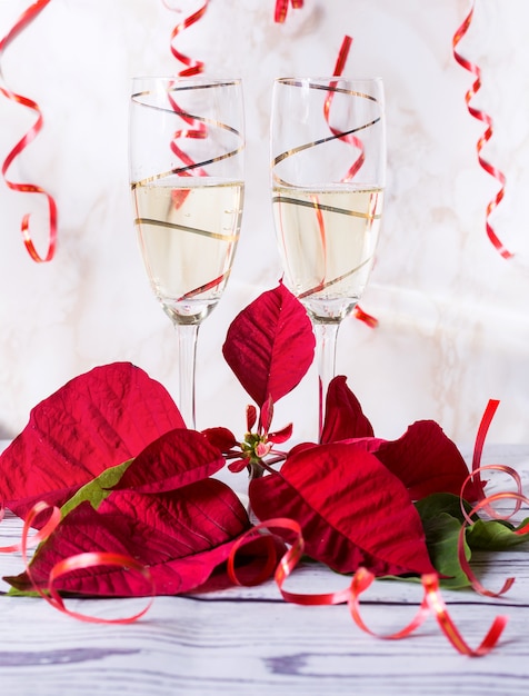 Twee gouden glazen vol champagne met poinsettia en streamers