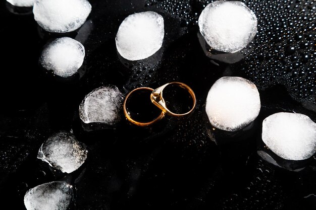 Twee gouden ringen op een zwarte achtergrond met druppels water en stukjes ijs