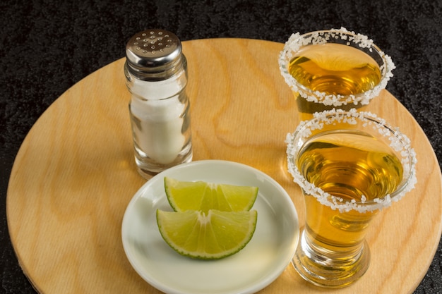 Twee gouden tequilaschoten op het ronde houten bord