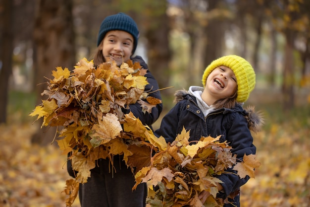 Twee grappige kleine meisjes op een wandeling in het herfstbos met herfstbladeren, wazige achtergrond, kopieerruimte.