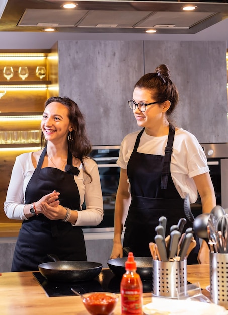 Twee grappige professionele vrouwelijke chef-koks die lachen en eten koken in een grote keuken