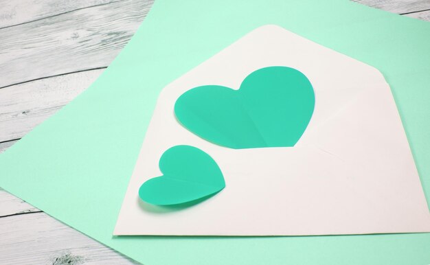 Twee groene harten in een witte envelop op mint kleur en houten achtergrond, een kopie van de ruimte, het concept van Valentijnsdag en liefdesverklaringen.