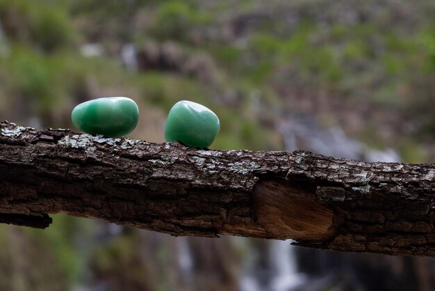 Twee groene kwartskristallen ondersteund door een boomtak met een wazige waterval op de achtergrond