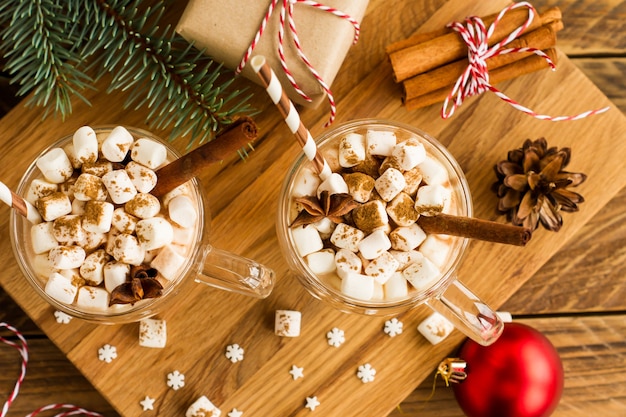 Twee grote haken met een chocoladedrank of cacao in een nieuwjaarscompositie met ballen, een geschenkdoos en kaneelstokjes. bovenaanzicht.