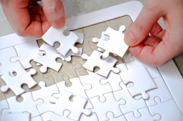 Twee hand met een stukje witte puzzel onvolledige puzzel op de tafel