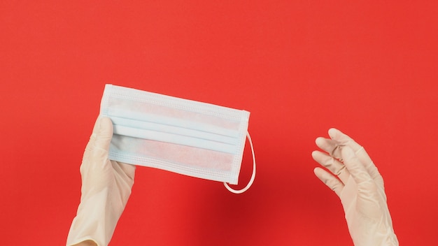 Twee handen dragen latexhandschoenen of witte medische handschoenen en gezichtsmasker op rode achtergrond.